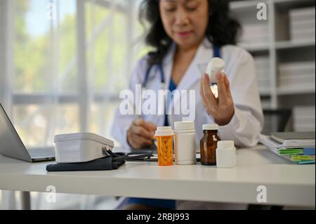 Close-up image of medicine bottles is on a doctor's office desk. A female doctor writing a medicine prescription at her desk in an examination room. Stock Photo