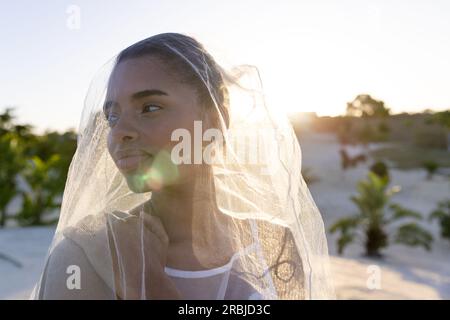 Closeup of beautiful biracial young bride wearing veil looking away at beach against clear sky. Copy space, unaltered, destination wedding, beach, eve Stock Photo