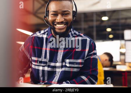 Portrait of happy african american businessman using phone headset and smiling at office. Business, confidence, communication and work. Stock Photo