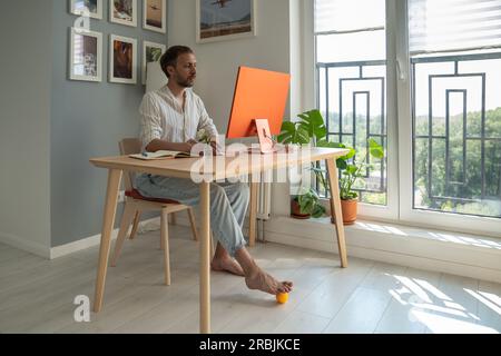 Young man freelancer using foot massager while sitting in front of computer Stock Photo