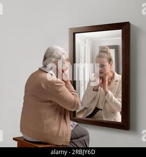 Creative conceptual college. Senior woman looking in mirror with reflection of her young self. Aging process Stock Photo