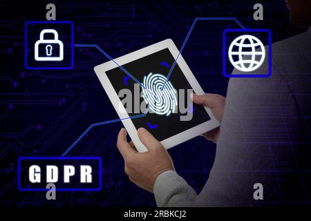 General Data Protection Regulation. Man holding tablet with fingerprint on screen against dark blue background with circuit board pattern, closeup. GD Stock Photo