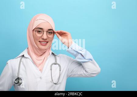 Muslim woman wearing hijab and medical uniform with stethoscope on light blue background, space for text Stock Photo