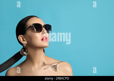 Stylish young woman with beautiful flower tattoo on turquoise background, space for text Stock Photo