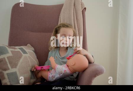 young girl feeding her doll at home Stock Photo
