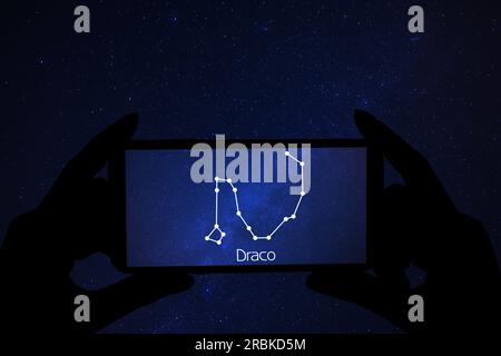 Woman using stargazing app on her phone at night, closeup. Identified stick figure pattern of Dragon (Draco) constellation on device screen Stock Photo