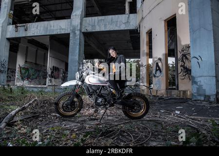 Woman posing on scrambler type motorcycle in abandoned building Stock Photo