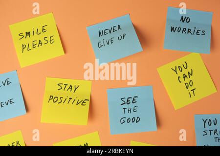 Paper notes with life-affirming phrases on pale orange background Stock Photo