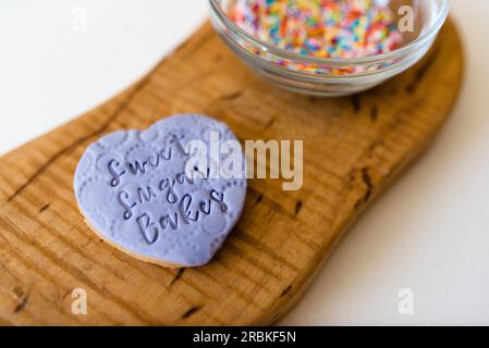 A heart shaped decorated cookie on a wooden board with sprinkles Stock Photo