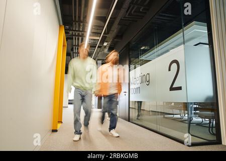 long exposure of two successful business partners walking along meeting room in corridor of contemporary office with coworking environment and high te Stock Photo