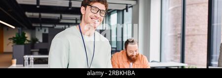 overjoyed and successful businessman in eyeglasses looking at camera while bearded architect working on new project on blurred background in modern de Stock Photo
