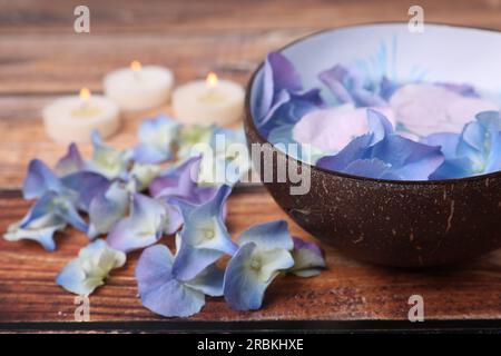 Spa composition. Aromatic water in bowl, burning candles and flowers on wooden table, closeup. Space for text Stock Photo