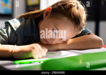 Caucasian schoolgirl sitting at desk and taking notes in school classroom Stock Photo