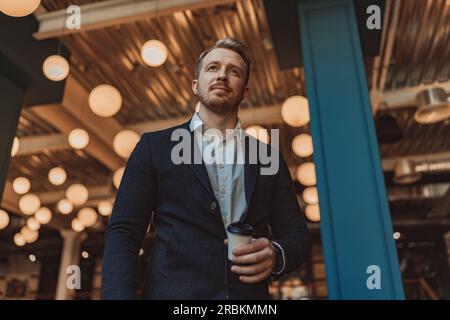 Portrait of handsome businessman in suit holding coffee cup and looking at side Stock Photo
