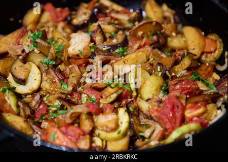 Food background with vegetable stew, ratatouille of roasted seasonal organic veggies sprinkled with fresh herbs, in a cast-iron pan. Vegetarian meal. Stock Photo