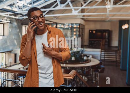 Young smiling freelancer talking by phone while standing on coworking background Stock Photo