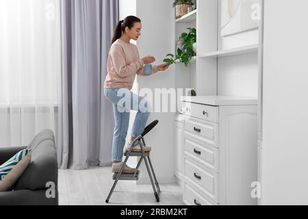 Woman on ladder watering houseplant at home Stock Photo