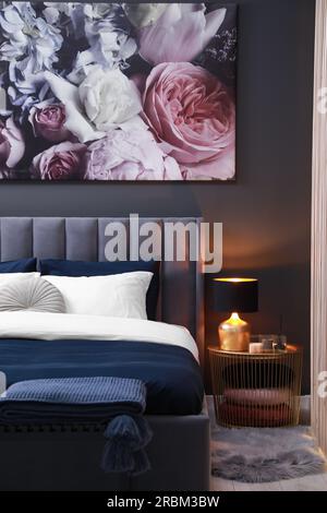 Comfortable bed with cushions, lamp and different decor on bedside table in room. Stylish interior Stock Photo