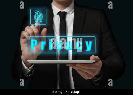 Privacy policy. Businessman activating privacy feature on virtual screen while holding tablet against black background, closeup Stock Photo