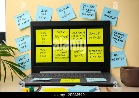 Paper notes with life-affirming phrases and laptop on table against beige background Stock Photo