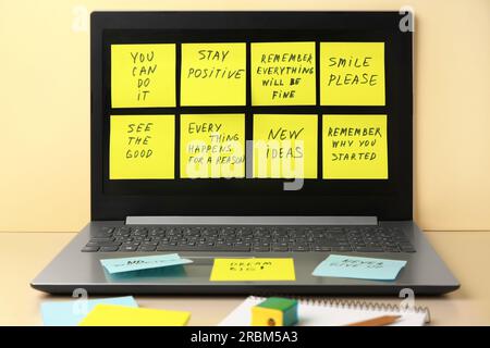 Paper notes with life-affirming phrases and laptop on table against beige background Stock Photo