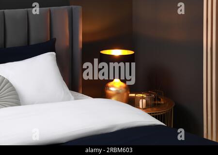 Comfortable bed with cushions, lamp and different decor on bedside table in room. Stylish interior Stock Photo