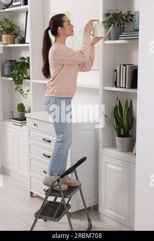 Woman on ladder watering houseplant at home Stock Photo