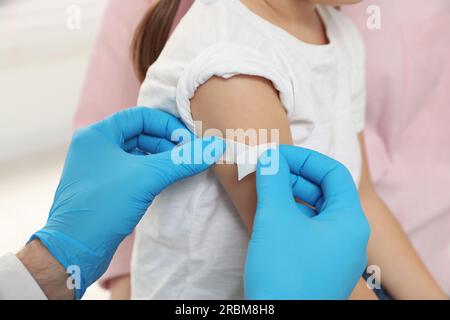 Children's hepatitis vaccination. Mother with her daughter. Doctor sticking medical plaster on little girl's arm, closeup Stock Photo