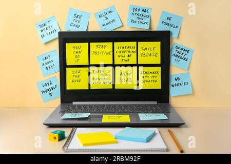 Paper notes with life-affirming phrases and laptop on table against beige background Stock Photo
