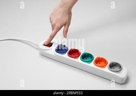 Woman pressing switch button of power strip on white background, closeup Stock Photo