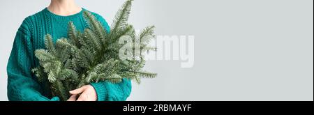 Women's in green pullover holding Christmas evergreen spruce Danish branches for make decoration. Festive decoration for Xmas holiday. Banner with cop Stock Photo