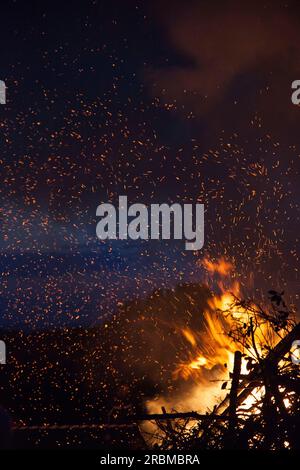 Sparks and embers fly from  a bonfire, creating tiny points of light against the night sky. Stock Photo