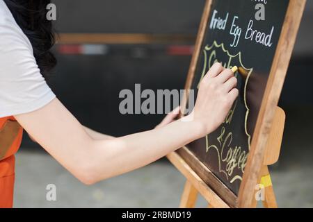 Closeup image of small business owner writing menu of street food cafe on chalkboard Stock Photo