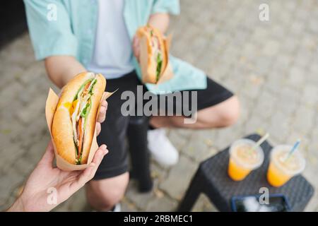 Couple eating sandwiches and drinking soda when having lunch in park Stock Photo