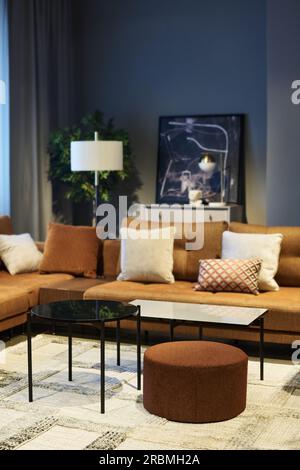 Two soft brown couches with cushions making corner in spacious room or coworking area with round table, bench and ottoman standing on carpet Stock Photo