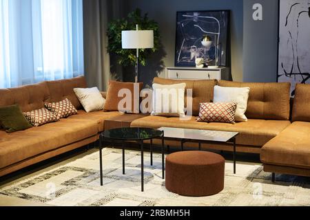 Corner of coworking area with soft comfortable couches with cushions standing in front of round table, brown padded stool and bench Stock Photo