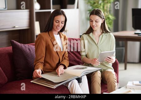Two young smiling female designers discussing textile samples in catalogue while one of them pointing at page during consultation Stock Photo