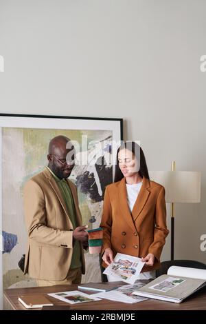 Two young creative designers of interior looking through collection of samples while choosing suitable color and textile for their new project Stock Photo