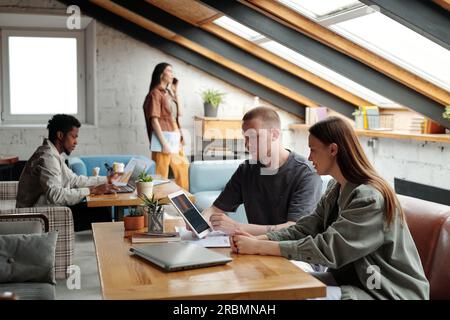 Young confident male manager with tablet making presentation of online data or project points to female colleague while sitting next to her Stock Photo