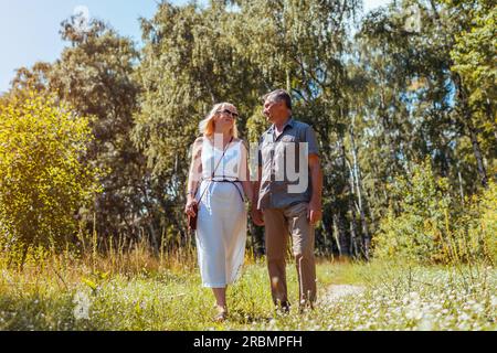 Senior family couple walking outdoors in summer forest. Elderly people holding hands. Romantic date. Man and woman enjoy landscape Stock Photo