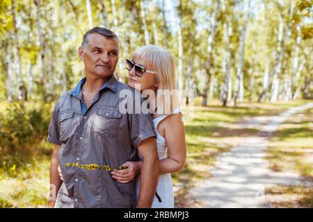 Portrait of senior family loving couple walking outdoors in summer forest. Elderly people hugging relaxing on date. Space Stock Photo