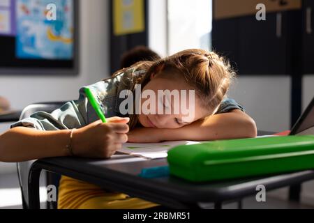 Caucasian schoolgirl sitting at desk and taking notes in school ...