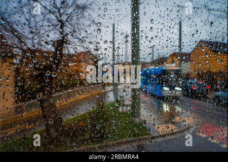 Raindrops on a window pane overlooking an intersection with moving cars and a tram, Jena, Thuringia, Germany Stock Photo