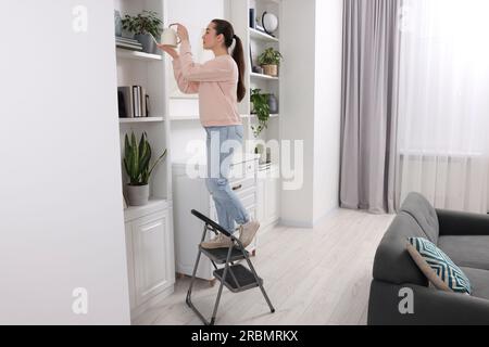 Woman on ladder watering houseplant at home Stock Photo