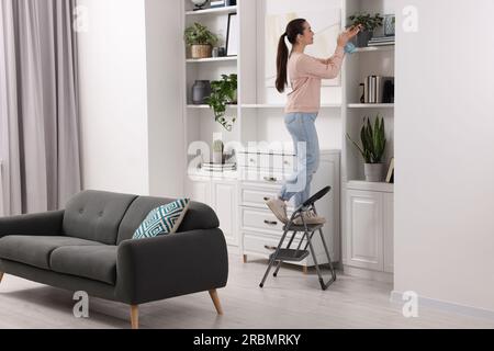 Woman on ladder watering houseplant at home Stock Photo