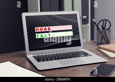 Choosing between hoax and fact. Laptop with words on wooden table in office Stock Photo