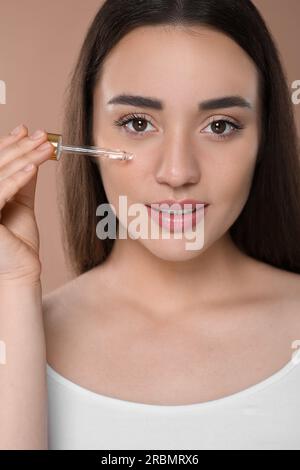 Woman applying essential oil onto face on brown background, closeup Stock Photo