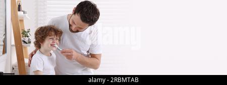 Father helping his son to brush teeth in bathroom. Banner design with space for text Stock Photo