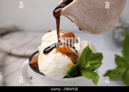 Pouring caramel sauce onto ice cream with candies and mint leaves, closeup Stock Photo