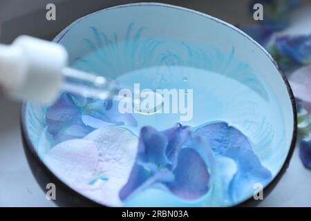 Dripping essential oil from pipette into bowl with water and flowers, closeup Stock Photo